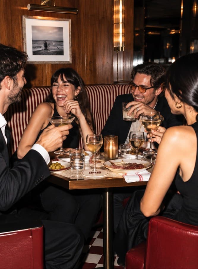 Friends laughing over drinks in a red leather booth with striped upholstery